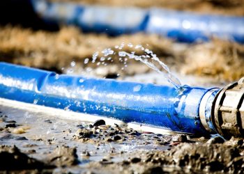 wasting water - water leaking from a hole in a hose. shallow dof with focus on leak