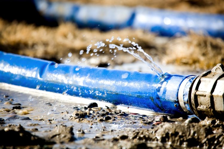 wasting water - water leaking from a hole in a hose. shallow dof with focus on leak